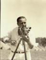 Harris Tuttle using movie camera while smoking pipe