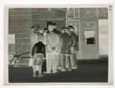 [Group of men and a newsboy reading notice in window of Rough & Caldwell painted backdrops store]