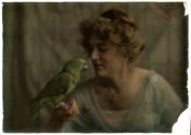[Woman in evening attire, green parrot perched on her thumb]