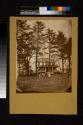 [Young woman with baby, two boys amd three little girls with dog and cart on front lawn of home]
