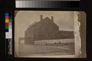 [Three story brick structure with three people sitting along fence]
