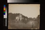 [Suburban stone house with four story tower, greenhouses in back]