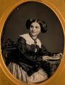 [Seated young woman with book on table]