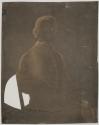 [Young man, seated in chair, holding a book]