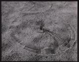 [Circle formed in sand by a grass stalk moved around by the wind]