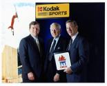 Bill Pressano, Colby Chandler and Ned Harkness standing in front of skier photo and Kodak sports sign. One of them is holding an ORDA sign