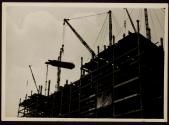 Steel beams are hoisted by derricks. Empire State
