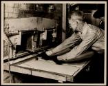 "Carrying-in-boy" (about 60 years old). Putting a paddle-load of glass stoppers from the "shop" that produces them into the "lehr" (annealing oven).