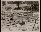 [Relief worker crossing riverbed]