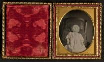 [Young child laid out in white gown]