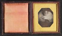 [Small deceased child, posed as if asleep, with hands crossed over chest]