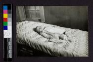 [Deceased baby laid out by grilled window]