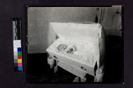 [Baby laid out in cloth-draped coffin]