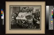 [Elderly woman laid out with "Sister" floral arrangements]