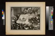 [Elderly woman laid out with "Sister" floral arrangements]