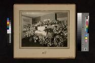 [Woman laid out in coffin with "Mother" floral arrangement]