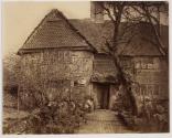 [Man sitting in the doorway of a cottage]