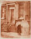 [Old woman walking in front of building]