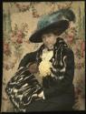 [Seated woman wearing dress with black and white furs and hat with blue feather]