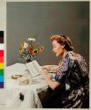 [Woman sitting at lunch reading a book, mouse "climbing" tablecloth]