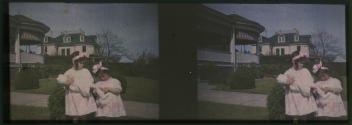 [Two girls with doll, houses in background]