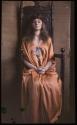 [Woman in gown, sitting in wooden throne]