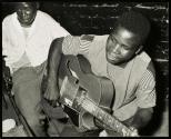 The dance music in this Bulawayo beer hall in Southern Rhodesia is furnished, at the moment, by a manufactured guitar. Home-made versions of string instruments are more common.  Almost inevitably, there are also drums.