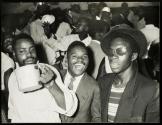 A beer hall in Bulawayo, Southern Rhodesia, serves its brew in massive tin mugs. Attire varies from the conventional European to mixed ensembles.