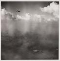 [Distant aerial view of ships at sea and an airplane]