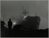 Transport ship docked in fog, sailor silhouetted in foreground