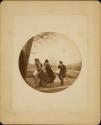 [Two women and a man, walking into wind, holding onto hats]