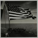[American flag against crowded deck of aircraft carrier]
