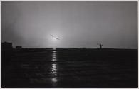 Hellcat Wings Home From France - In an impressive "black and white" photograph, a Navy Grumman Hellcat is guided to a landing aboard the deck of its carrier by the Signal Officer in the early morning of f Southern France, August 15, 1944.