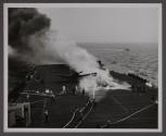 As streams of water play upon the fire, it shrinks away to steam and smoke, leaving the charred skeleton of the wing of the HELLCAT visible in the haze.
