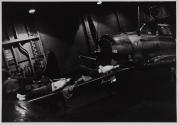 [Two men sleeping by airplanes on hangar deck]