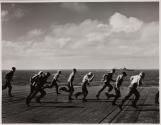 [Group racing down dock, ship beyond]