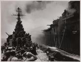 [Ship spraying water on burning aircraft carrier at sea]