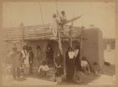 [Native Americans standing in front of adobe building]