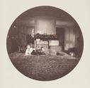 [Interior, boy and girl lying on oriental rug in front of trunks]