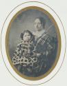 [Young mother holding an apple, with child on her lap]