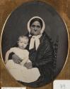 [Elderly woman, seated in chair, holding a child]