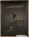 [Profile of a woman sitting in a chair holding a book in her lap]