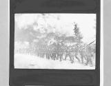 ZW. German soldiers marching through a village after setting fire.
