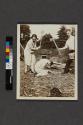 [Man and woman with axes posing above kneeling woman]