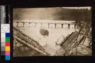 [Large group in boat near ruined bridge]