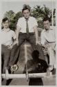 [Three men posing on hood of car]