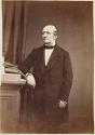 [Man with arm resting on pedestal]