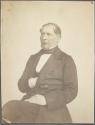 [Seated man with hand tucked in vest]
