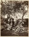 [Two women and man chopping wood]