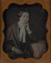 [Woman leaning on table with hand to face]